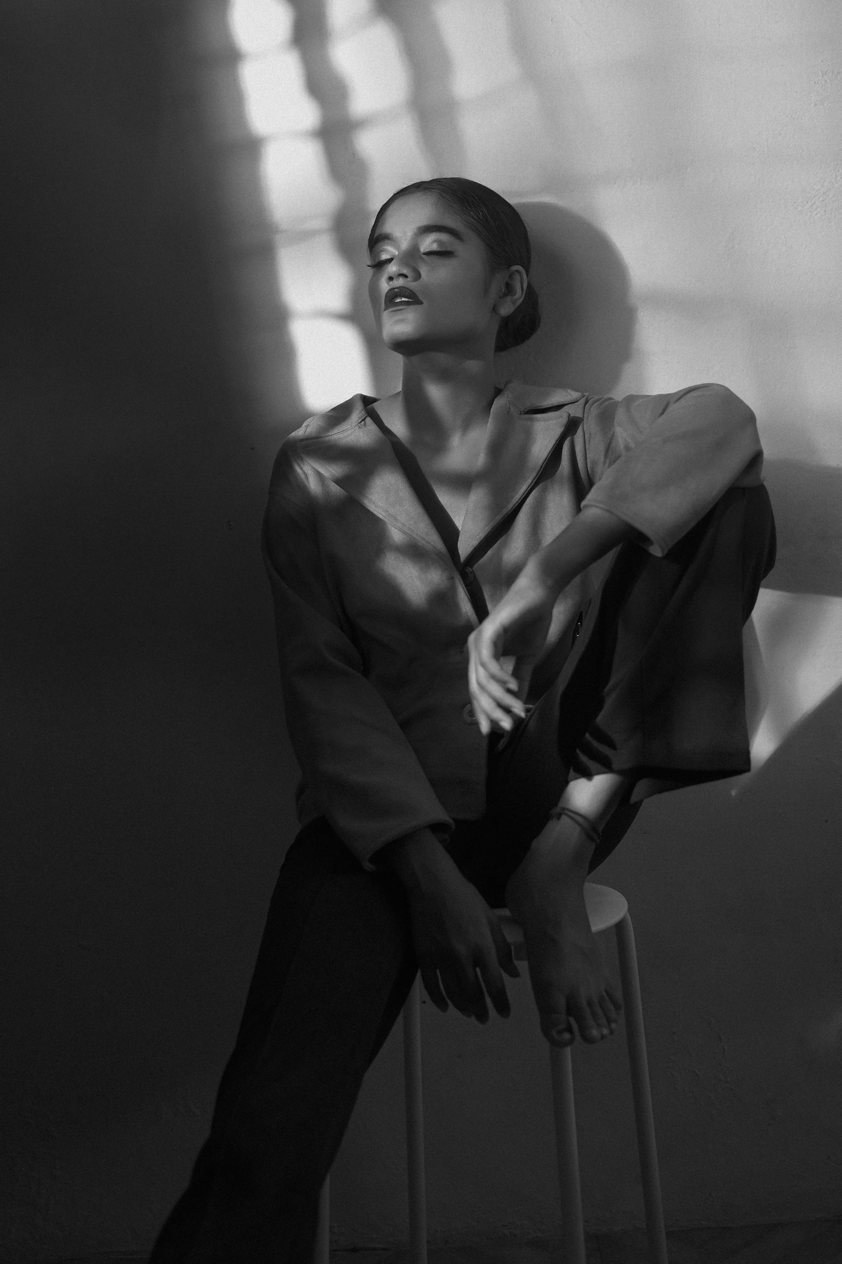 Elegant black and white portrait of a model sitting in shadow, showcasing artistic expression and moody lighting.